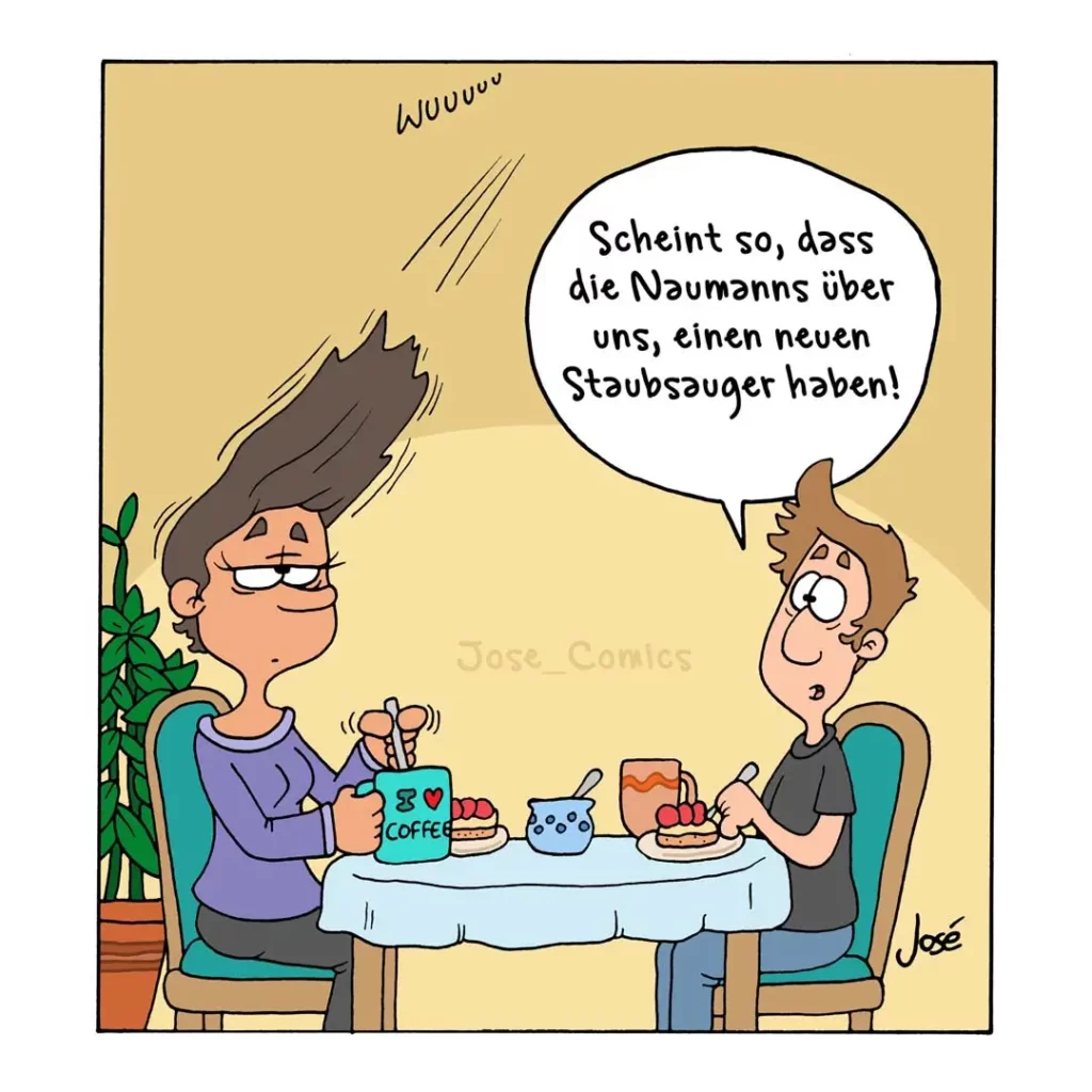 Zwei Personen sitzen sich an einem Tisch gegenüber, eine Person mit erhobenem Haar sagt lachend etwas, der andere wirkt entsetzt und hält sich den Mund zu