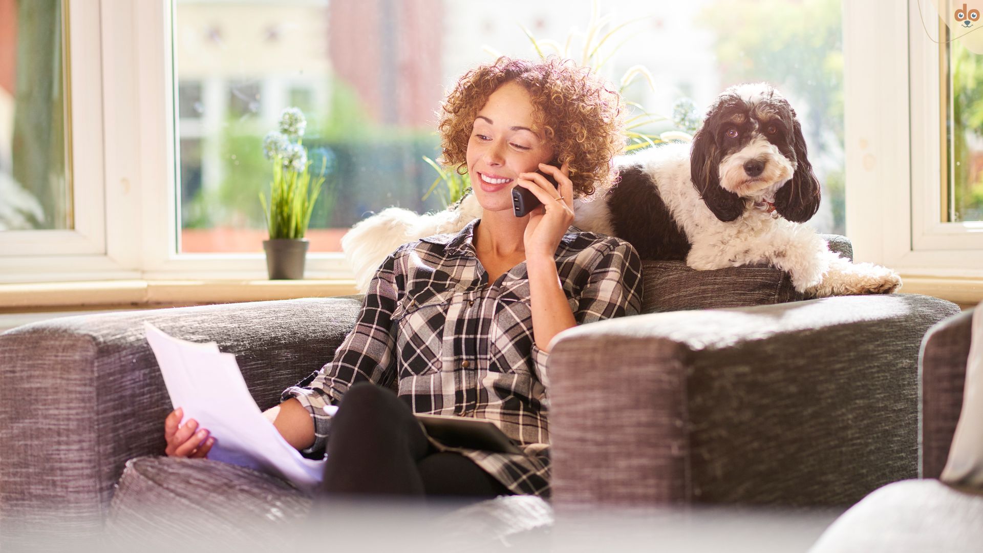 Frau sitzt mit ihrem Hund auf dem Sofa und telefoniert mit Hundehaftpflichtversicherung