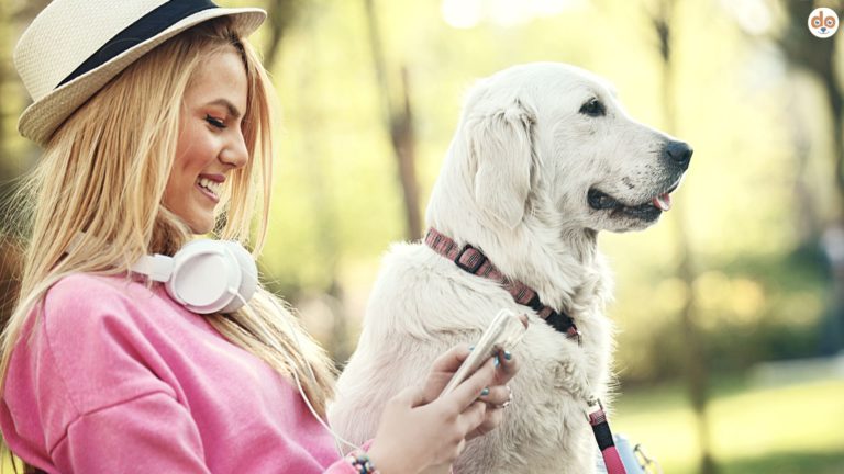 Frau mit Smartphone und Kopfhörer beim Gassi mit ihrem Hund