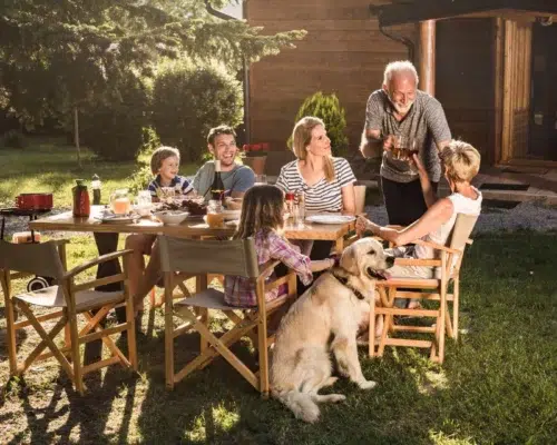Familienhund beim gemeinsamen Essen draussen im Garten, Ferienhaus Holzhaus im Hintergrund